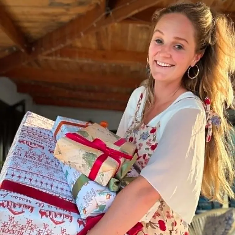 Ella smiling with an armful of presents wrapped in Holy Homes paper and red ribbon